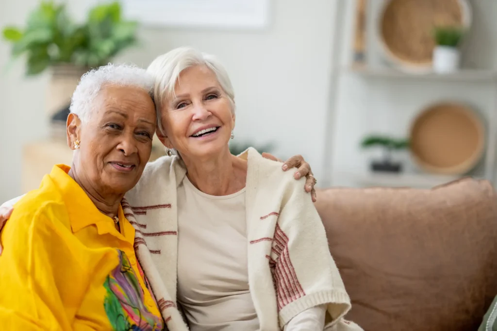 Two senior friends sit together on a sofa in their retirement residence.